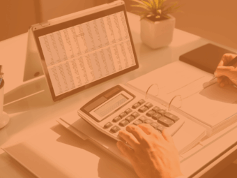 Person working on invoices at a desk, with papers, a laptop, and a calculator visible.