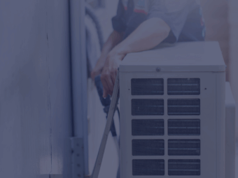A maintenance technician checking an AC unit inside an apartment during summer